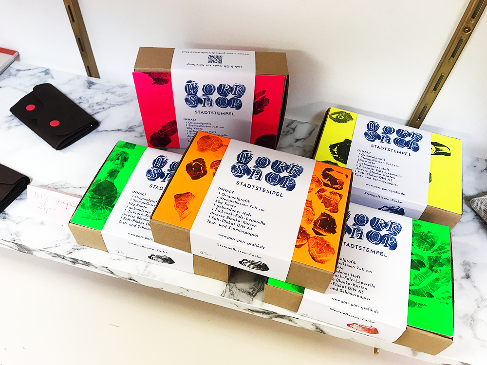 5 Stadtstempel-Workshop-Boxen  in verschiedenen Neon-Farben liegen im Regal