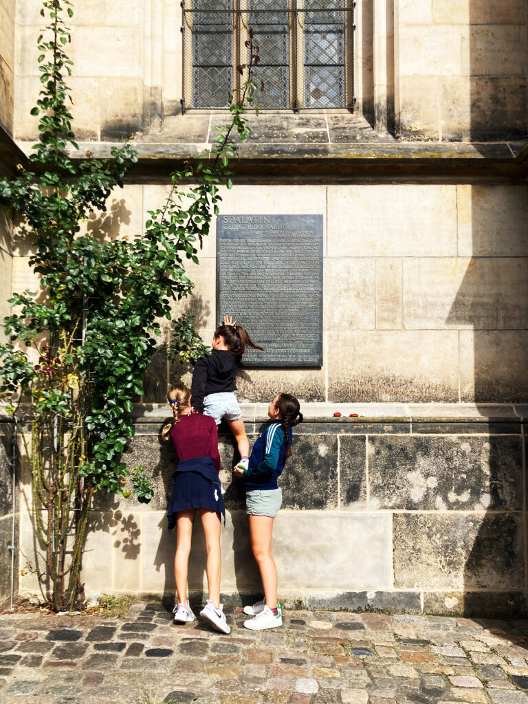 Stadtstempel-Workshop in Altenburg: zwei Teilnehmer:innen stemmen eine:n Teilnehmer:in empor, um einen Knetstempel an einer Kirchenfassaden-Schriftafel zu erstellen. 